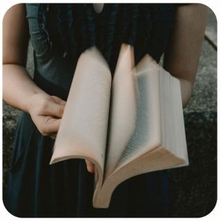 Frau blättert in einem Buch. Link zu unserem Onlineschaufenster Langes Wochenende.